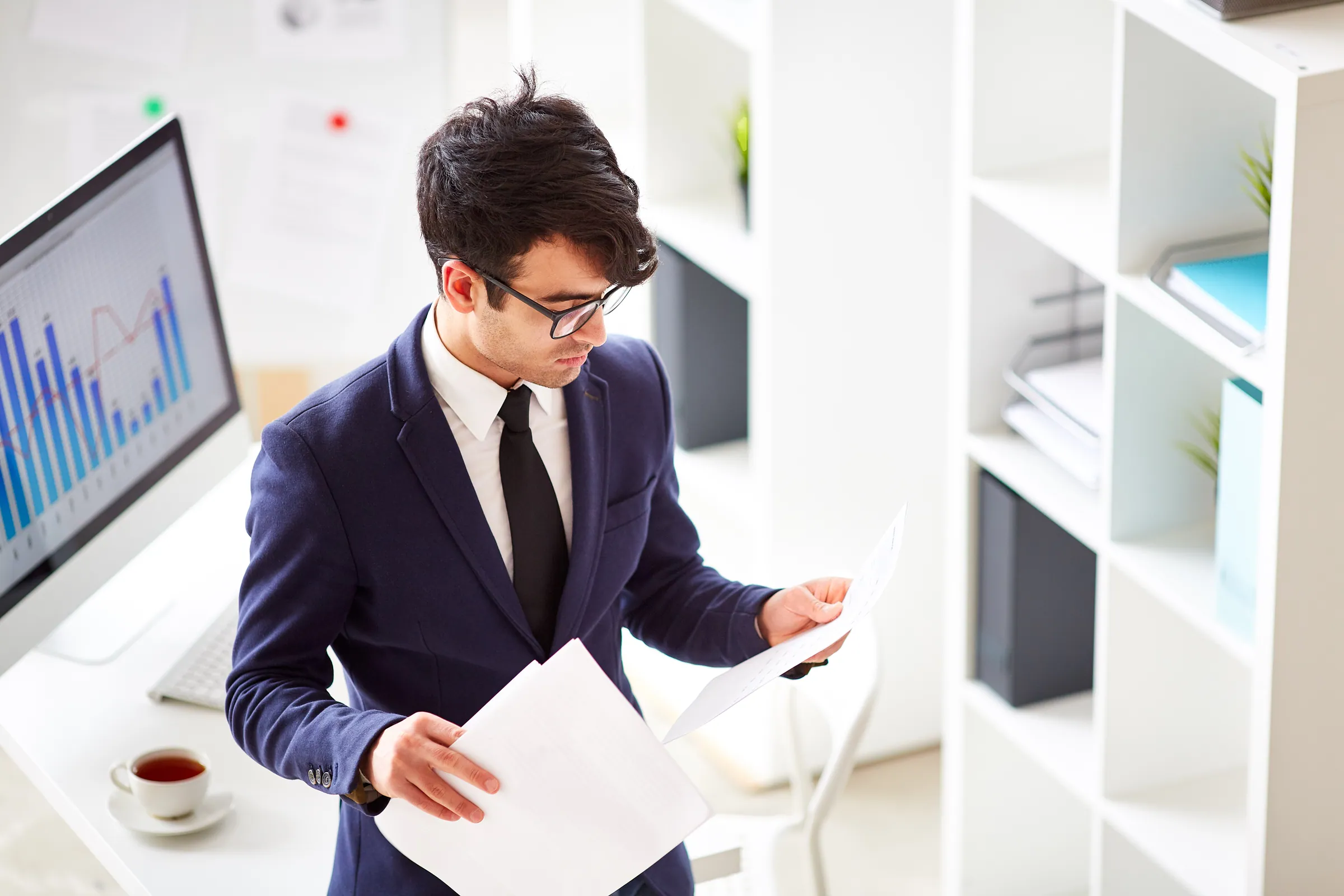 Accountant in a navy suit reviewing financial statements beside chart monitors, representing tax and accounting technology