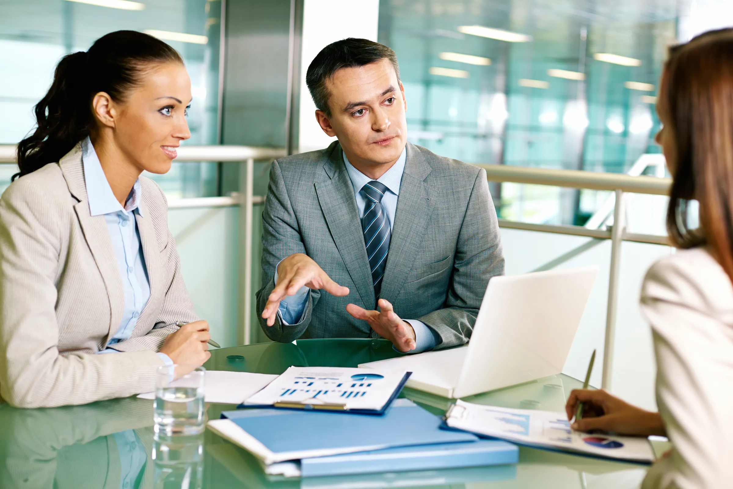 Two advisers in business suits briefing a client across a desk, representing banking, finance and insurance technology