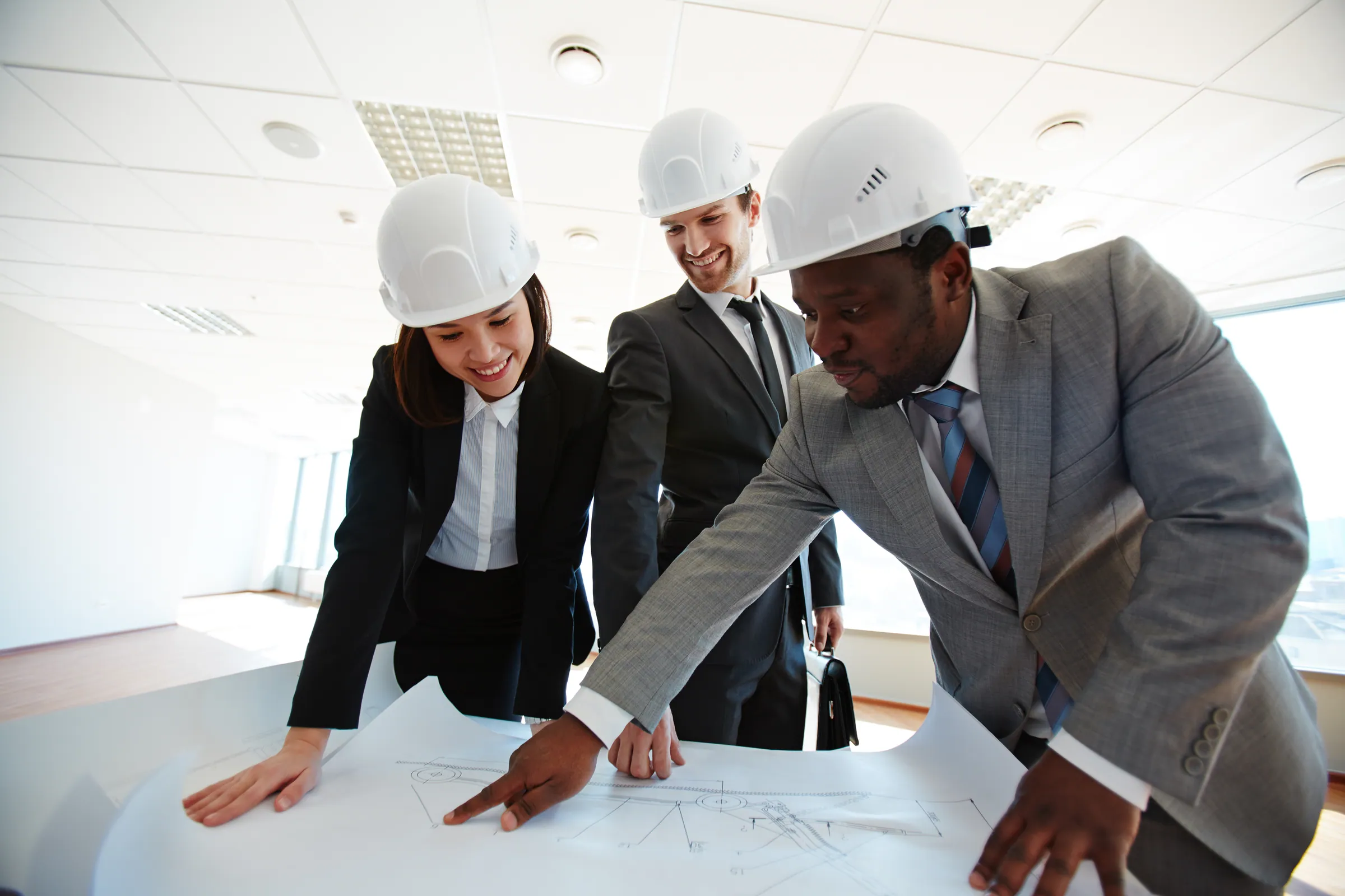 Three colleagues in business suits and hard hats reviewing drawings together