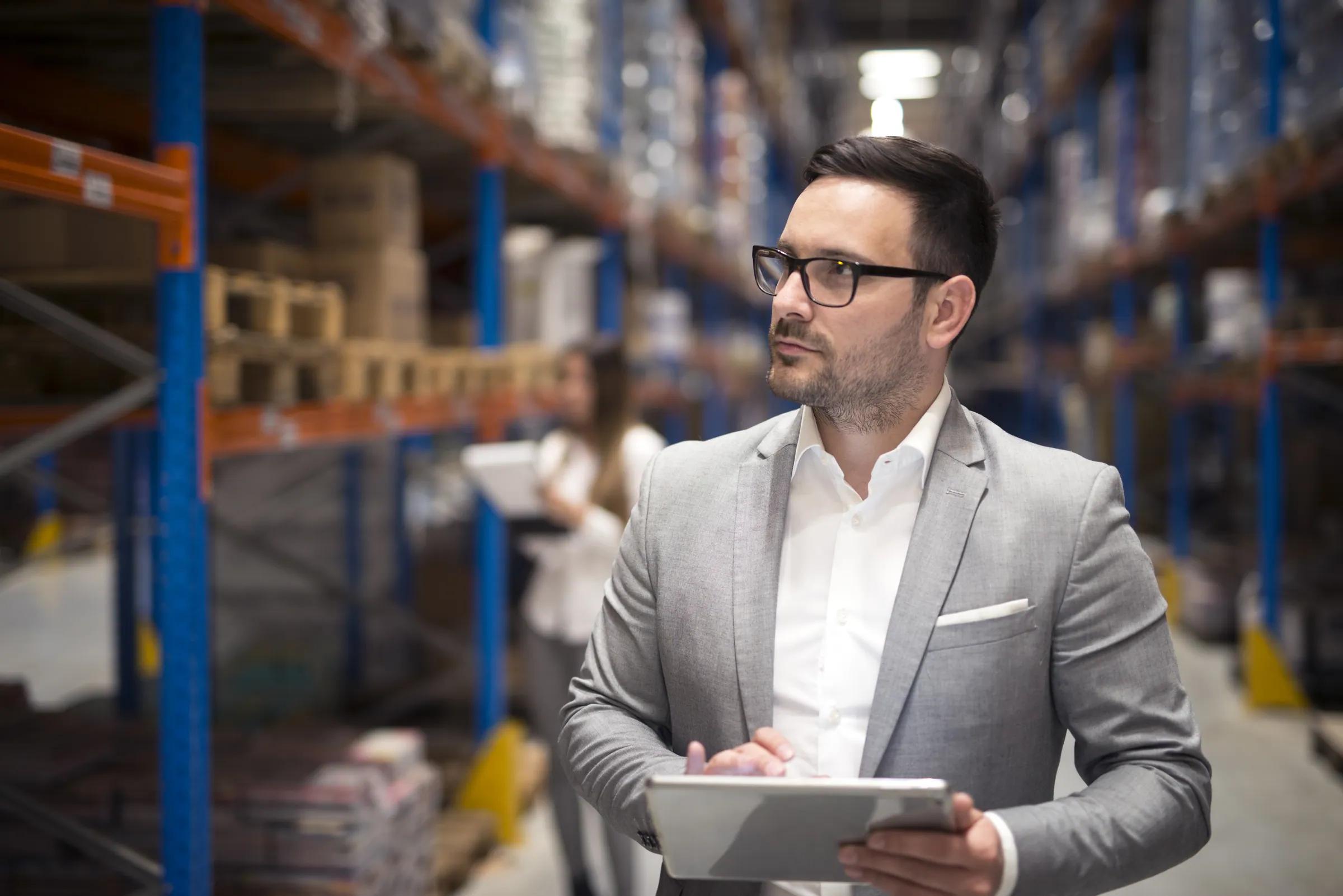 Manager in a suit reviewing stock on a tablet in a warehouse aisle