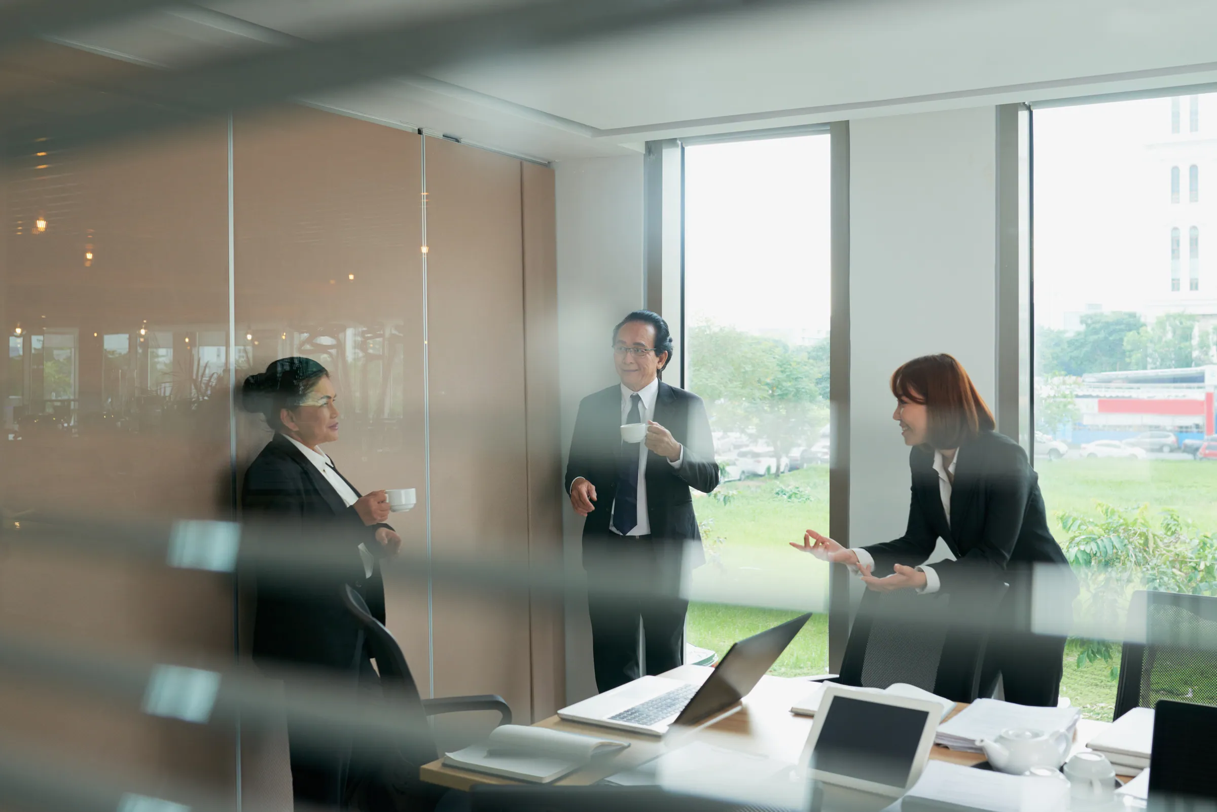 Three colleagues in dark business dress in a glass meeting room