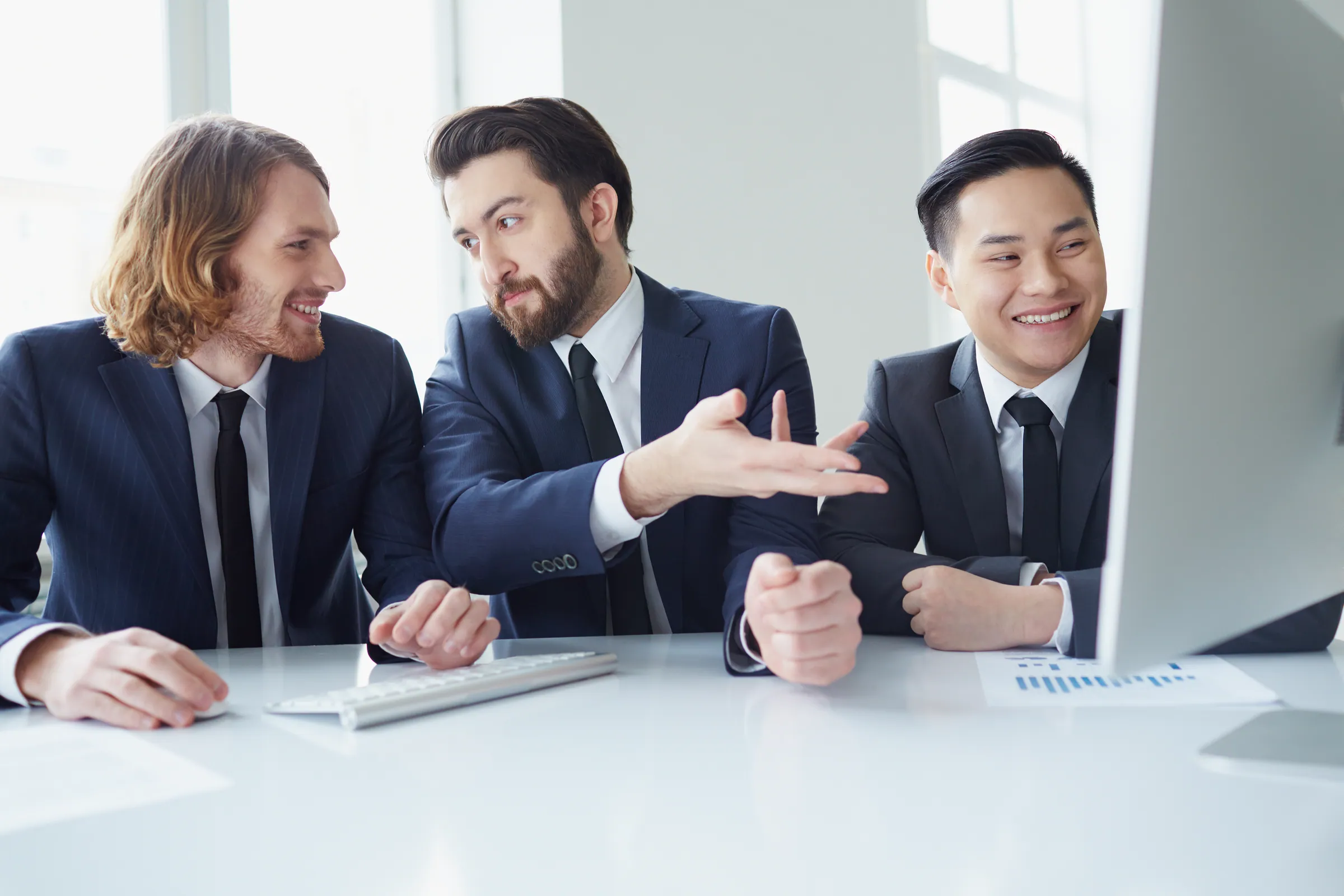 Three colleagues in suits working at a shared screen