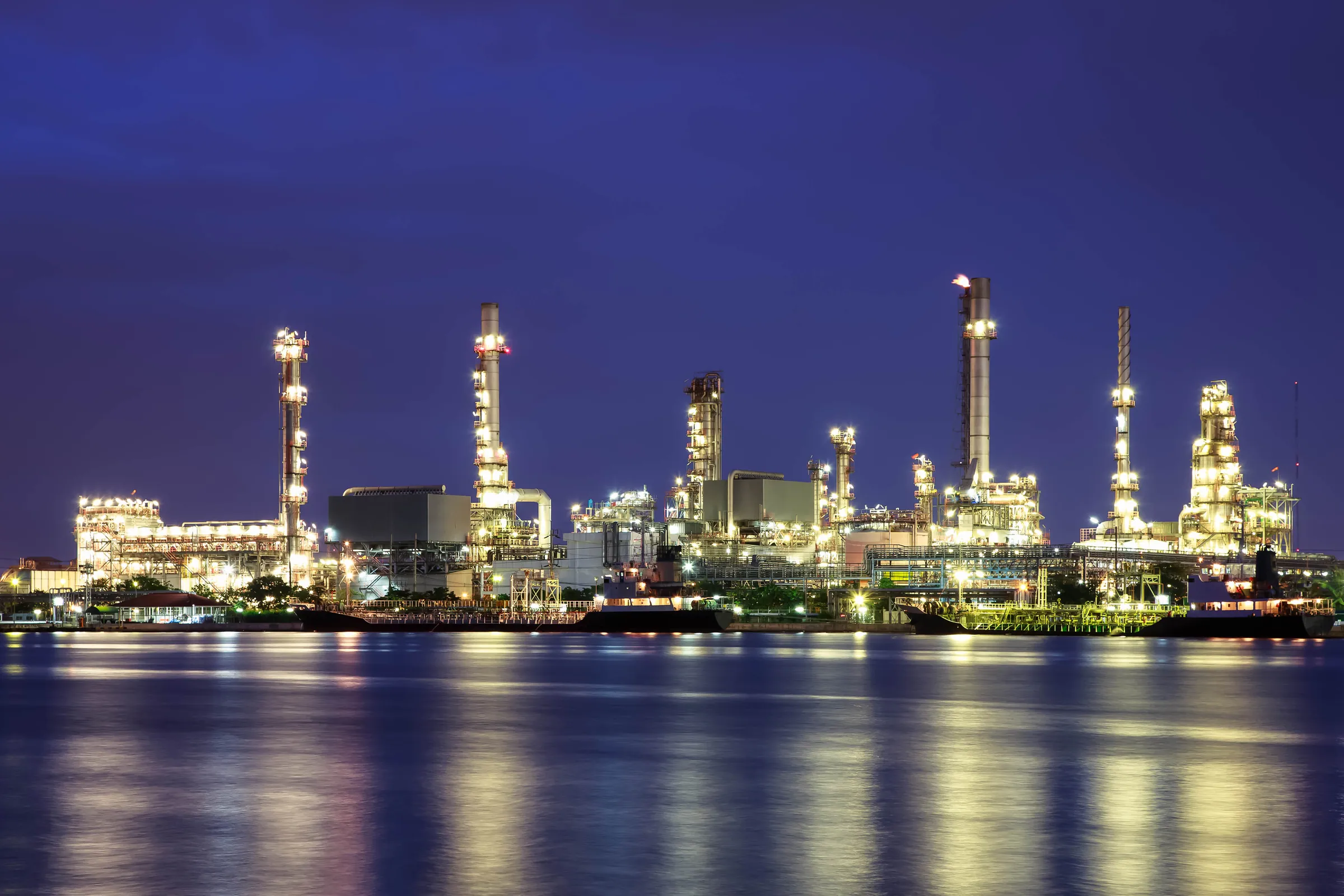 Oil refinery lit at twilight reflected in water