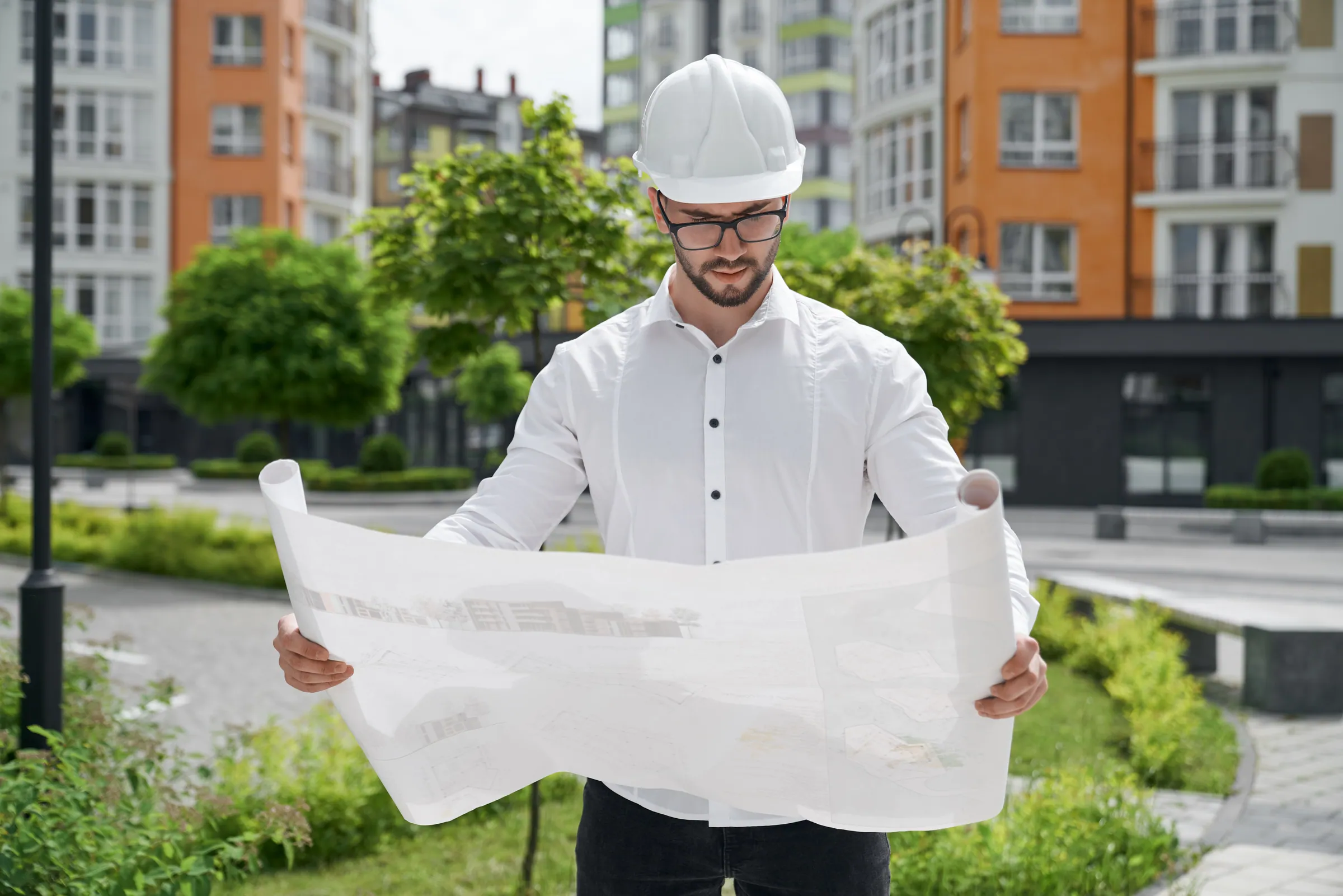 Engineer in a hard hat reading plans in front of a development
