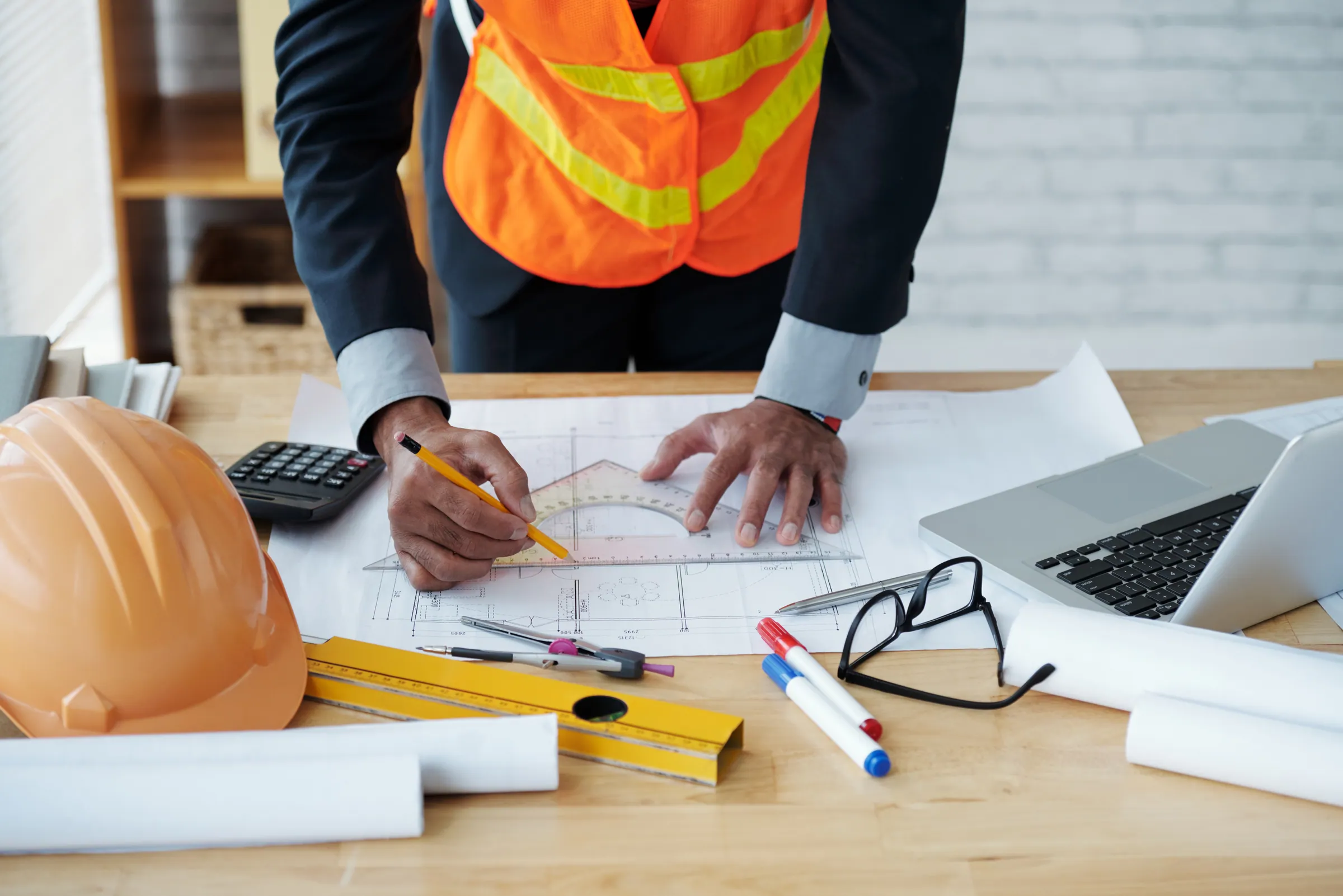 Man in a suit and hi-vis drafting over building plans