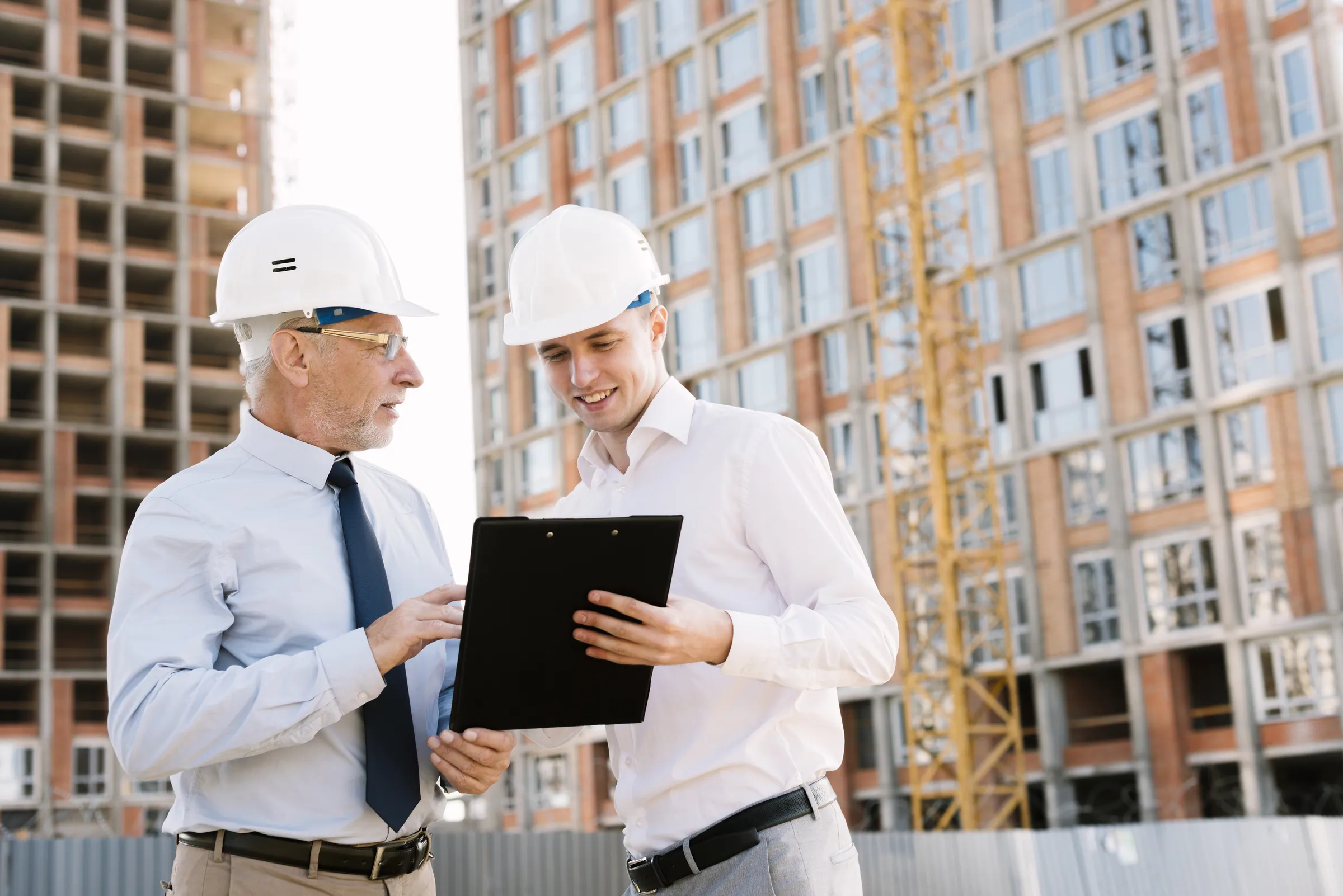Two colleagues in hard hats reviewing a clipboard on site