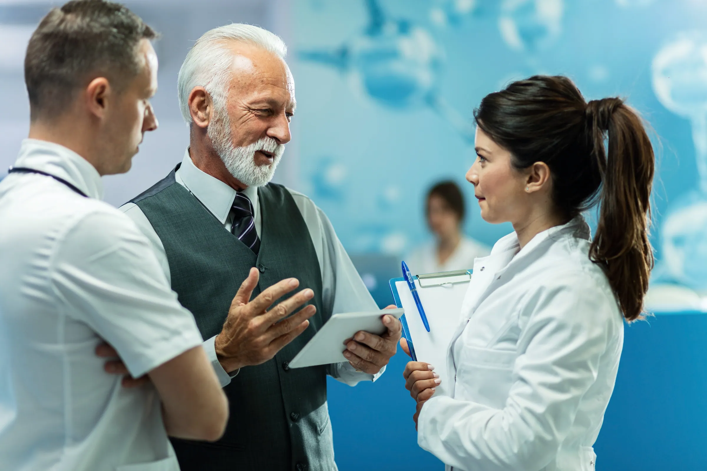 Executive with a tablet briefing clinicians in a corridor