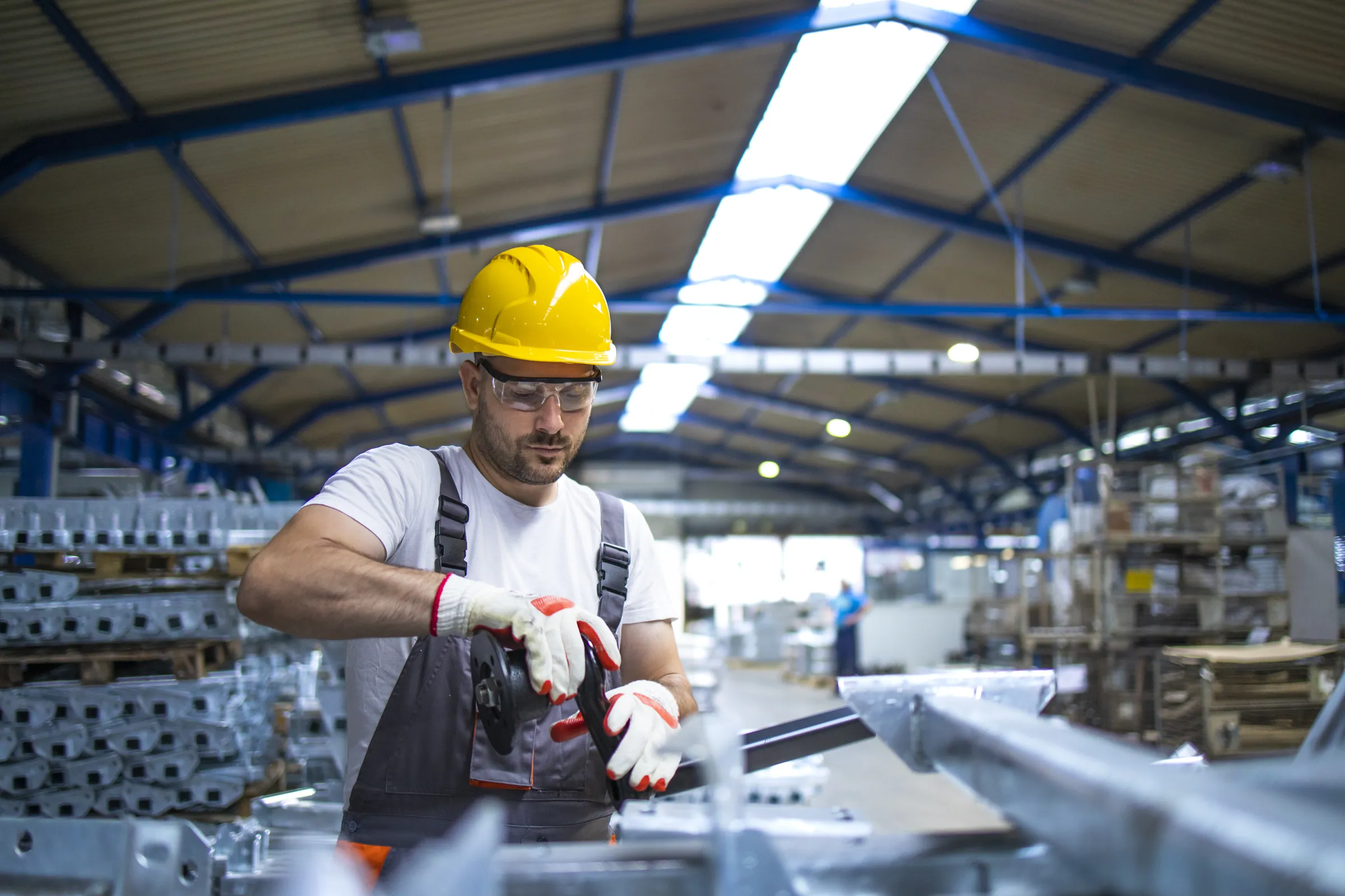 Factory worker in a yellow hard hat with an angle grinder